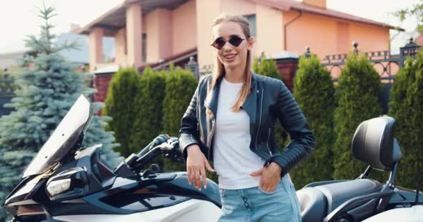 주차장에 오토바이 근처에 선글라스를 매력적인 여자는 카메라 미소를 슬로우 — 비디오