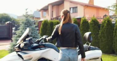 Siyah ceketli genç bir kadın bisiklete biniyor. Bisikletli kız. Motosikletli kız. Şoför Hanım. Spor ve ulaşım. Sarışın sürücü. Spor motosikletli güzel bir kız. Yavaş çekim.