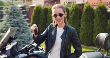 Yakın plan. Kendine güvenen bir kadın yeni bir motosiklet alır. Gülümseyen beyaz kız yeni spor bisiklet anahtarları tutuyor. Yavaş çekim.