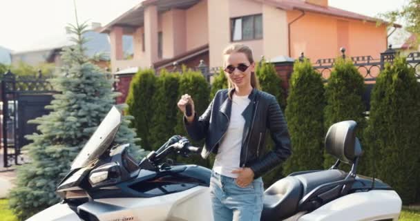 一个快乐迷人的骑摩托车的女人 戴着太阳镜 把钥匙放在她的新摩托车上 站在街上 慢动作 — 图库视频影像