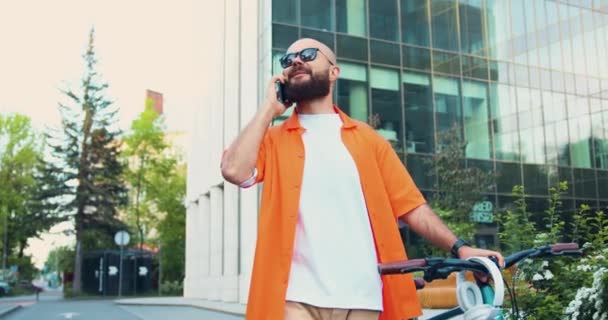 Pozytywny Hipster Człowiek Pomarańczowej Koszuli Okularach Przeciwsłonecznych Wpisując Smartfonie Podczas — Wideo stockowe