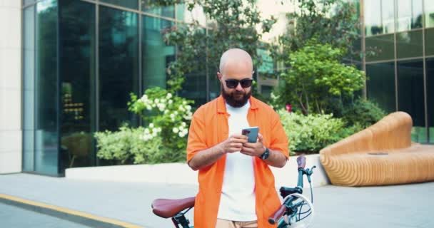 オフィスセンター近くの自転車で歩いている間 スマートフォンを使ったハンサムな男 都市の環境に優しい輸送 魅力的なマネージャー個人アシスタントサイクリング通勤 環境に優しい車両 — ストック動画