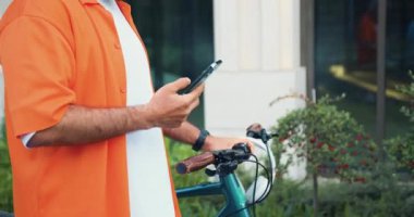 Ofis merkezinde bisikletle yürürken akıllı telefon tutan erkek elleri. Şehre çevre nakli. Bisiklet sürerken sohbet etmek. Modern yaşam tarzı, bağlantı. Meşgul insanlar için modern aletler. Yavaş
