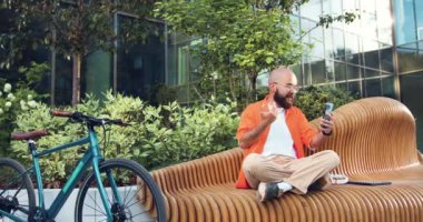 İnternetteki son moda hippi şehirli adam akıllı telefon kullanıyor, dışarıda bisikletin yanında oturuyor. Serbest çalışan bir ofis çalışanı, iş adamı, iş adamı. Yavaş çekim.
