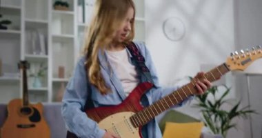 Uzun kıvırcık saçlı, uzun kıvırcık saçlı, gitar çalan, evdeki ışık odasında şarkı söyleyen ve dans eden genç kız. Kamera hareket ediyor, yavaş çekim.