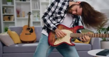 Uzun saçlı, elektro gitar çalan, dans eden ve müzik stüdyosunda başını sallayan heyecanlı genç adam, yaşam tarzı. Yavaş çekim