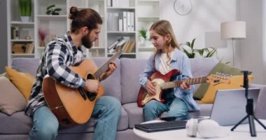 Müzik öğretmeni ve genç kız kanepede oturup açık oturma odasında ya da müzik stüdyosunda özel derste gitarla yeni şarkı çalmayı öğreniyorlar. Yavaş çekim