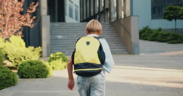 一个学生背着背包跑到室外阳光街上的现代学校大楼 小学生沿着城市街道的人行道跑去上学 儿童的概念 — 图库视频影像