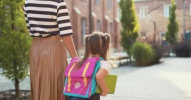 Arkaya bakan genç bir kadın beyaz elbiseli küçük bir kızı kendi elleriyle tutuyor. Şehre, ilköğretim okuluna gidiyor. Sırt çantalı kız öğrenci açık havada okula gidiyor. Aile okula geri döndü. Küçük kız gidiyor.