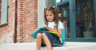 Okul çantasıyla okul merdivenlerinde oturmuş, gülümseyen ve notlar yazan lillte kız örgülerinin portresi. Sırt çantalı bir çocuk ders kitaplarını elinde tutuyor. Okula dönelim. Eğitim