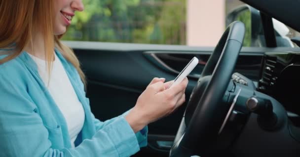 坐在司机座位上边开车边笑边用智能手机打字的少女 集中精神的女商人在车里用手机的侧视图 慢动作 — 图库视频影像