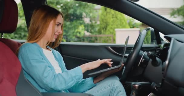 高級車でラップトップコンピュータで働く成功した女性の肖像画 彼女の車の運転席で友人から通勤する女性 彼女のラップトップとプレミアム車の車輪の後ろに座っている若い女の子 — ストック動画