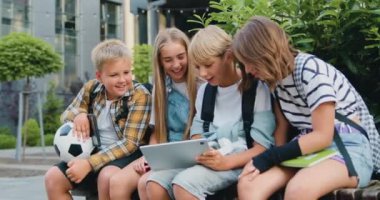 Mutlu oğlanlar ve kızlar birlikte tablet kullanırlar. Okuldan sonra bankta otururken gülümserler. Okula dönelim. Arkadaşlık okulu öğrencileri kavramı. Yavaş çekim