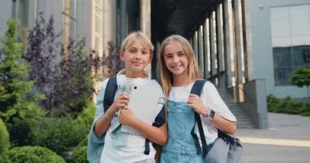 2人の美しい中学生の男の子と女の子の肖像画は 学校の建物の近くに立って ポーズし カメラを見ています 学校に戻って 友情コンセプト スローモーション — ストック動画