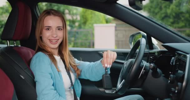 坐在车上的女人高兴地拿着钥匙 想在车上买辆新车 迷人的女孩从她的新车里拿着一把钥匙 微笑着唱着 慢动作 — 图库视频影像