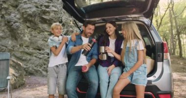 Baba, anne ve oğul ormanda kayaların yanında arabanın bagajında oturup termostan çay içiyorlar. Aile ve çocuklar doğada piknik yapıyorlar. Sonbahar sezonunda seyahat. Yavaş