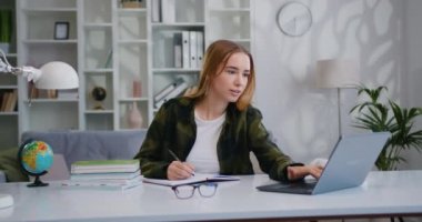 İç işlerinde çalışırken dizüstü bilgisayar kullanan genç iş kadını. Genç bayan planlama günü, organizatörde toplantılar, öğrenci defterinde notlar tutması, webinar izlemesi.