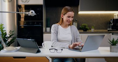 Portrait of beautiful caucasian female in stylish cozy living room using laptop computer at home. Girl browsing the Internet and checking videos on social networks, freelance work clipart