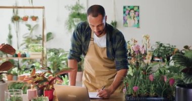 Çiçekçi dükkanındaki yeşil bitkileri kontrol eden önlüklü bir adam ve sonuçları bir deftere kaydediyor. Çiçek serasında çalışan çiçekçi müdürü. İnsanlar ve iş kavramı. Yavaş çekim.