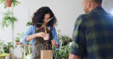 Afro-Amerikalı kadın çiçekçi paketleri kese kağıdına sarılıp erkek alıcıya hediye olarak çiçek almayı öneriyor. Çiçekçi kadın, ev bitkisi satıyor. Küçük işletme, ev dekorasyonu.