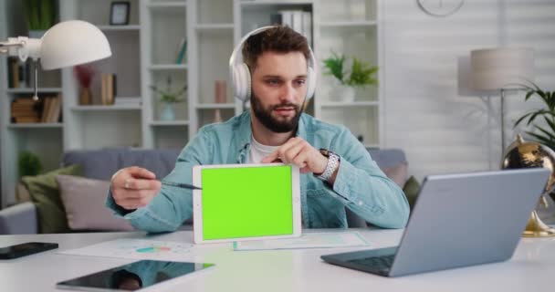 成功した白人男性は パートナーとのオンラインチャット中に緑色のタブレットを保持しています 彼女のタブレットのクロマキーを使用して男性フリーランサーは ビデオ通話で同僚とのオンラインミーティングを行います — ストック動画