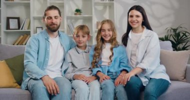 Baba, anne ve iki sevimli çocuğun aile portresi. Kameraya gülümseyen ve modern oturma odasında kucaklaşan. Kanepede oturan yakışıklı beyaz kadın ve erkek cadı oğlan ve kız.