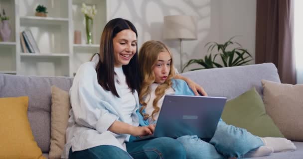 ハッピーな女性とかわいい子供の少女は 現代の部屋でラップトップを使用して楽しんで話しています コンピュータを搭載した教育 家庭でのソファーのサポートと指導 スローモーション — ストック動画
