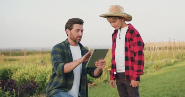 タブレットを使用して息子に結果を示し 高い5を与えます 幸せな家族の農夫の父と10代の息子は 分野でデジタルタブレットで働いています 農業ファームコンセプト スローモーション — ストック動画