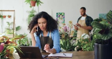 Önlüklü Afro-Amerikalı kadın, müşterisiyle cep telefonuyla konuşuyor ve bilgisayarcı adam kullanıyor. Aile çiçekçileri dizüstü bilgisayar kullanıyor, daktilo ediyor ve konuşuyor.