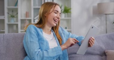 Gülümseyen beyaz kadın kanepeye oturmuş dijital tableti e-öğrenim için kullanıyor, faturaları internet üzerinden ödüyor, e-ticaret, uzaktan çalışma, evdeki oturma odasında sosyal medya. Yavaş çekim