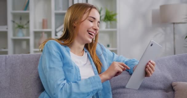 Χαμογελώντας Καυκάσια Νεαρή Γυναίκα Κάθεται Στον Καναπέ Χρησιμοποιώντας Ψηφιακή Ταμπλέτα — Αρχείο Βίντεο