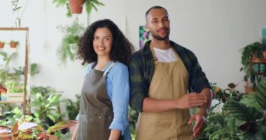 Önlüklü iki güzel ve profesyonel çiçekçinin portresi. Küçük çiçekçi dükkanında kameraya gülümsüyor. Afrika kökenli Amerikalı çift kamera önünde poz veriyor. Aile işi ve...