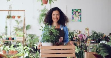 Çiçekçi dükkanında elinde çiçeklerle kameraya gülümseyen çekici Afrikalı Amerikalı kadın portresi. Kadın bahçıvan serada çiçeklerin arasında çalışıyor. Küçük bir iş. Yavaş çekim