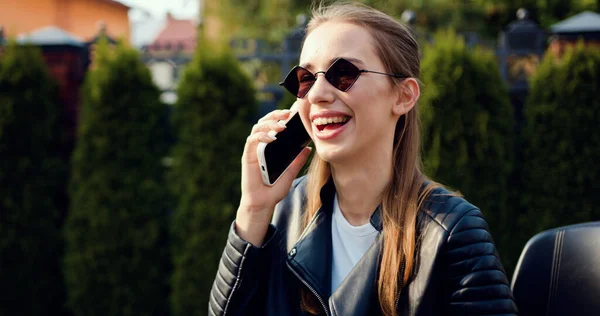 Güzel görünümlü, güneş gözlüklü, siyah elbiseli, lüks bir motosiklette oturan ve telefonda konuşan mutlu bir kadının portresi..