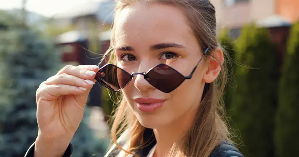 Güneş gözlüklü çekici bir kadının portresi binaların arka planında gülümsüyor. Yakın plan, gülümseyen ve kameraya bakan kız..