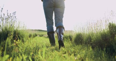 Kauçuk çizmeli çiftçi dışarıda, tarlada. Tarımcı olarak kara toprak üzerinde yürüyorum. Gün batımında filizlerle tarla boyunca yürüyen çizmeli kadın çiftçi bacakları. Küçük aile