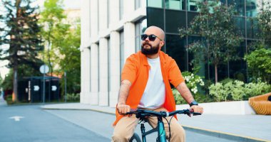 Güneş gözlüklü genç sakallı hippi işe giderken bisiklet sürüyor. Şehir gezgini konsepti. Yakışıklı sakallı yönetici başarılı CEO işe bisikletle gidip geliyor..