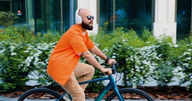 Kulaklıklı beyaz bir adam ve sabahları ofise giderken şehir duvarında bisiklet süren şık bir giysi..