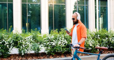Genç hippi sabah işe giderken akıllı telefon kullanıyor modern bisikletiyle. Ulaşım, iş ve sağlıklı yaşam tarzı kavramı.