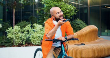 Gözlüklü hippi modern şehir sokağındaki cep telefonuna sesli mesaj kaydediyor. Bisikletiyle telefona odaklanmış profesyonel sesli mesaj kaydediyor..