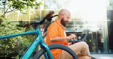 Modern çağın gözlüklü şehirli adamı ofisten bilgisayarla yedek kulübesinde oturuyor. İnternet üzerinden iş ve serbest projeler hakkında uygulama kullanan bir adam.
