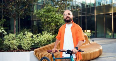 Bisikletinde gözlüklü genç beyaz adam portresi. Şehir sokağında kameraya bakıyor..