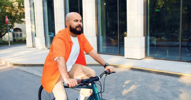Şehir merkezinde bisiklet süren yakışıklı, sakallı, gülümseyen adam. Profesyonel genç erkek şehir caddesinde bisikletle işe gidiyor..