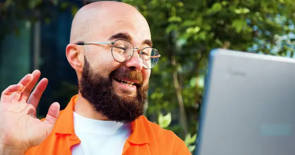 Smiling man freelancer in glasses working remotely online with headset and laptop. video call or distances meeting. Bearded male talking on distance remote conference by laptop online.