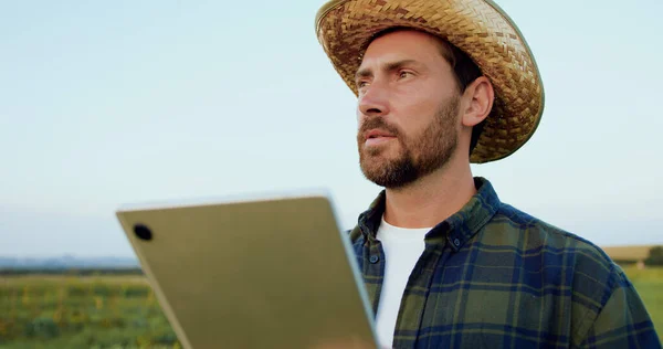 Young man farmer standing near field and looking around cheking information on tablet. Worker agronomist working on field with digital tablet, agriculture. Lifestyle agriculture business concept.