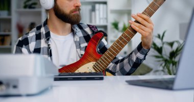 Sakallı sakallı bir müzisyen gitar çalıyor. Laptop, kulaklık ve internet müzik dersleriyle masada oturuyor. Kafkasyalı genç gitarist müzik enstrümanı çalışıyor