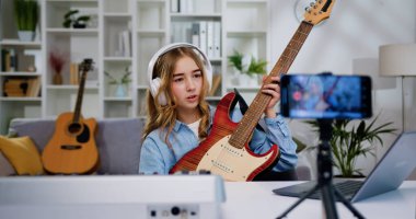 Ev telefonunda modern akıllı telefondan elektro gitar çalmak için video dersi alan genç ve güzel bir blog yazarı. İnternet işitme cihazı için elektro gitarın nasıl çalındığını gösteren kız.