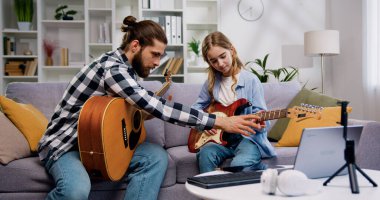 Müzik öğretmeni ve genç kız kanepede oturup açık oturma odasında ya da müzik stüdyosunda özel derste gitarla yeni şarkı çalmayı öğreniyorlar.