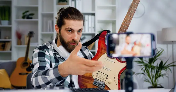 Male teacher blogger recording video class tutorial for play electric guitar on modern smartphone at home studio. Man showing how play for electric giutary for internet auditory
