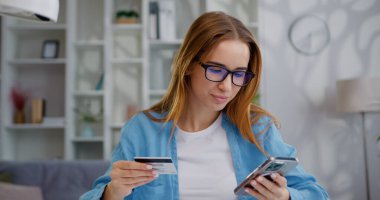 İş kadını evde cep telefonuyla online alışveriş yaparken masada oturuyor. Ödeme için elinde kredi kartı ve cep telefonu olan kız güvenli bankacılık hizmeti uygulaması ile internette